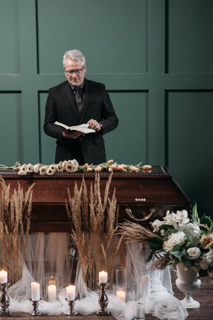 A pastor presides over a funeral ceremony with a coffin surrounded by flowers and candles, creating a solemn atmosphere.